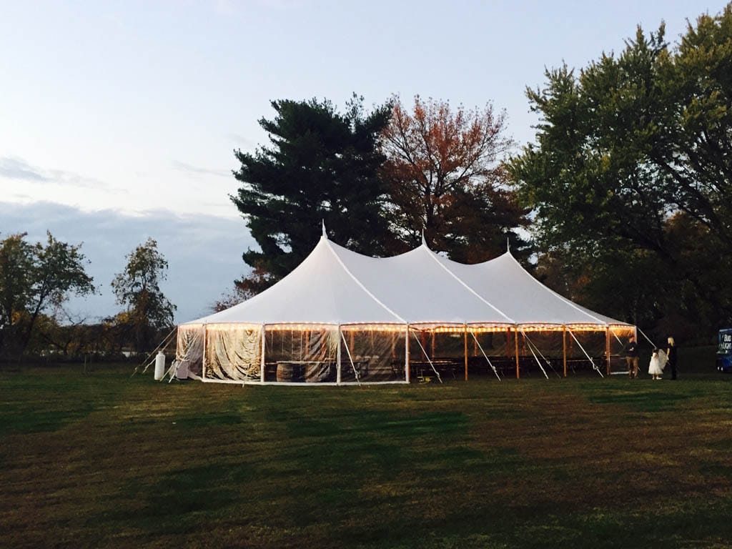 Sailcloth event tent with high peaks set up on a grassy field at sunset.