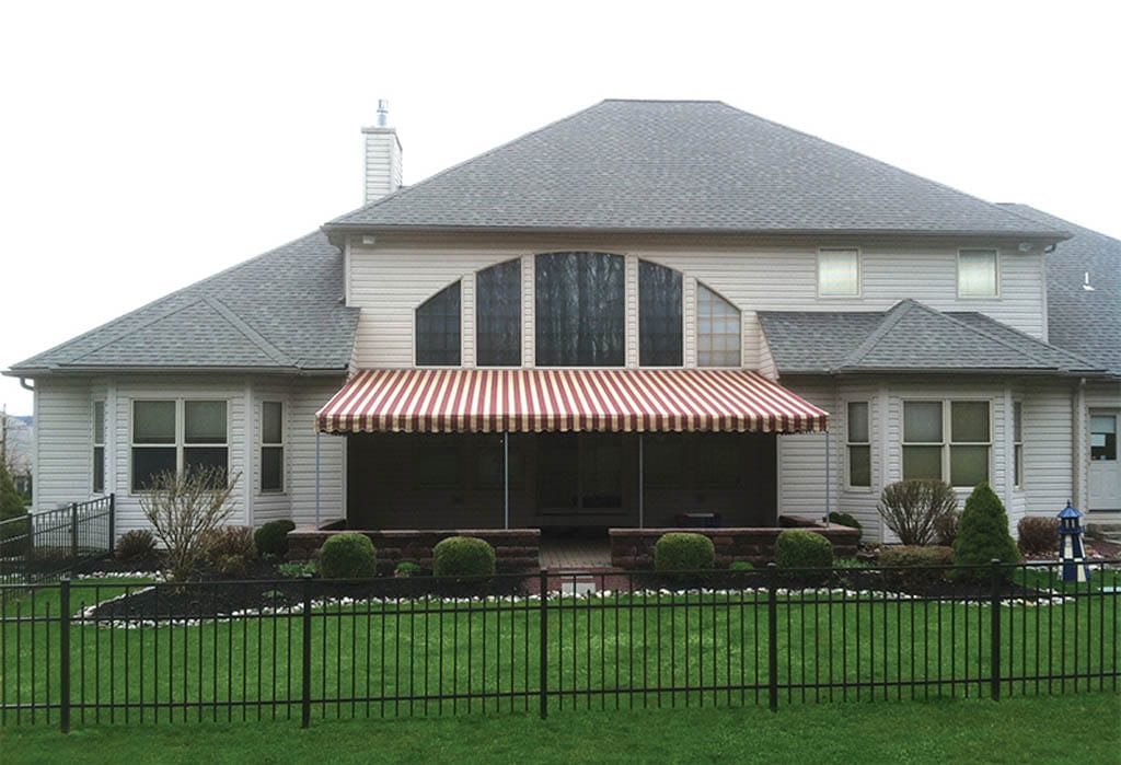 Backyard home with retractable red and white awning over a deck area.