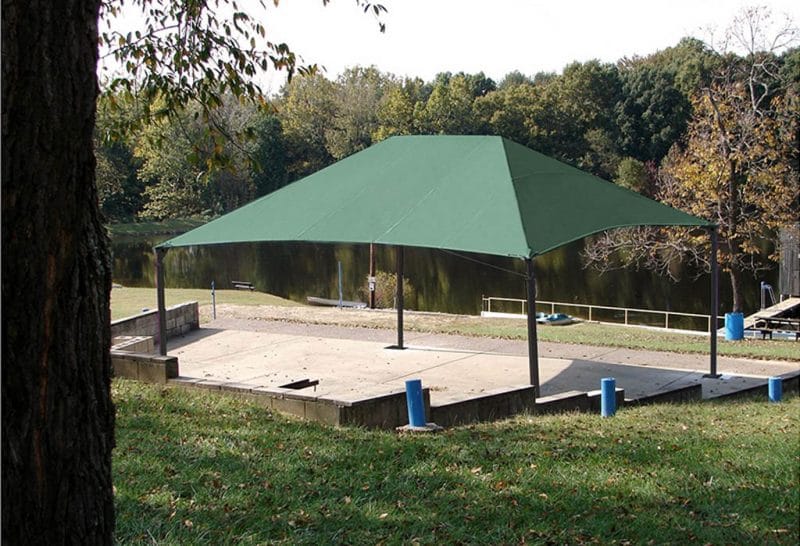 Green square shade canopy covering picnic tables in a park setting.