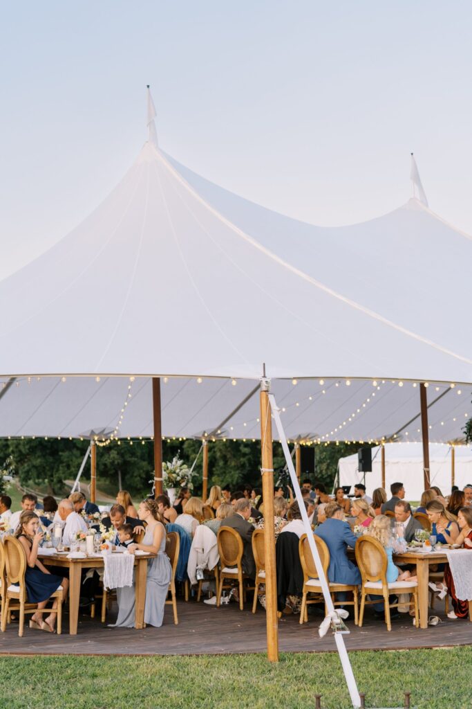 Elegant sailcloth tent setup for an outdoor event with wooden poles and lighting.