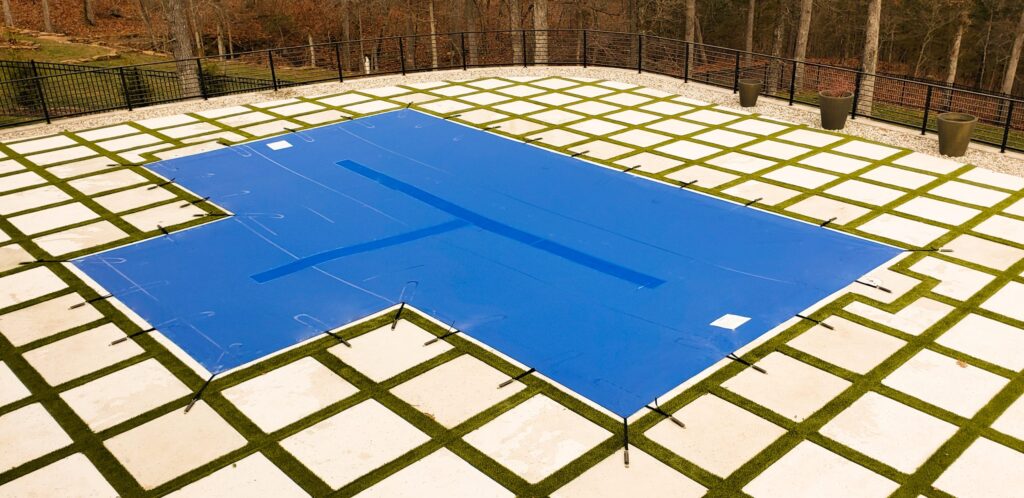 Backyard pool with bright blue mesh cover and stone patio.