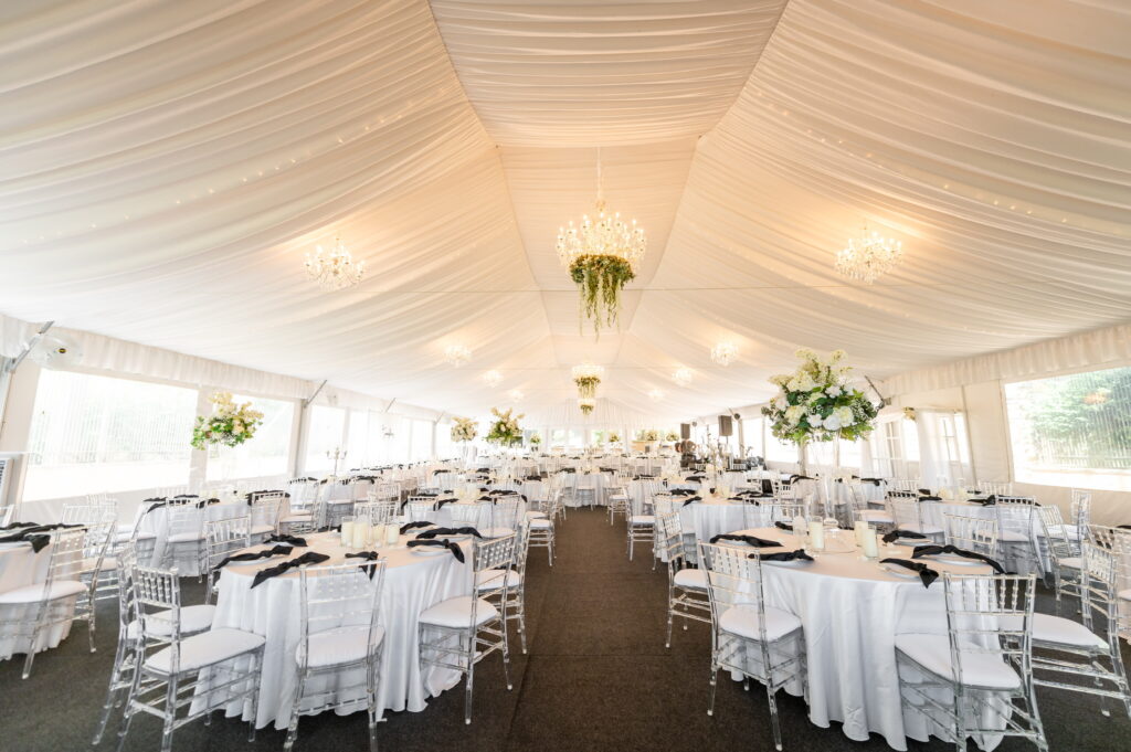 White event tent interior with chandeliers and rows of decorated dining tables.