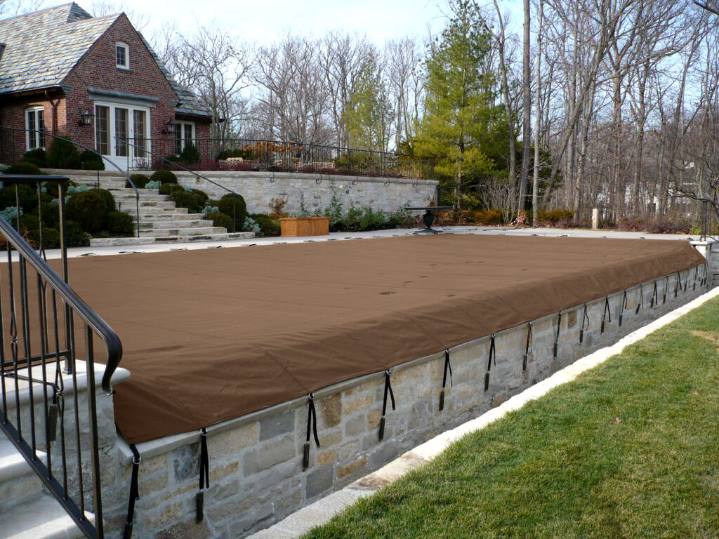 Long rectangular pool covered with a brown mesh safety cover.