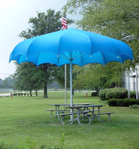 Blue umbrella shading a picnic table on a green lawn.