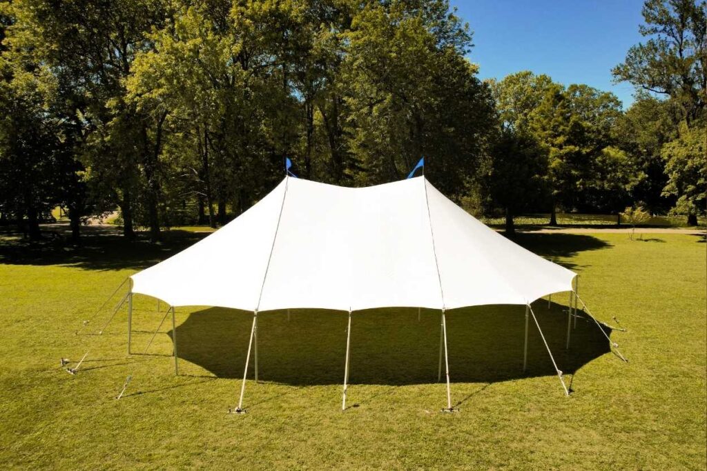 White pole tent set up on a grassy field for an outdoor gathering.
