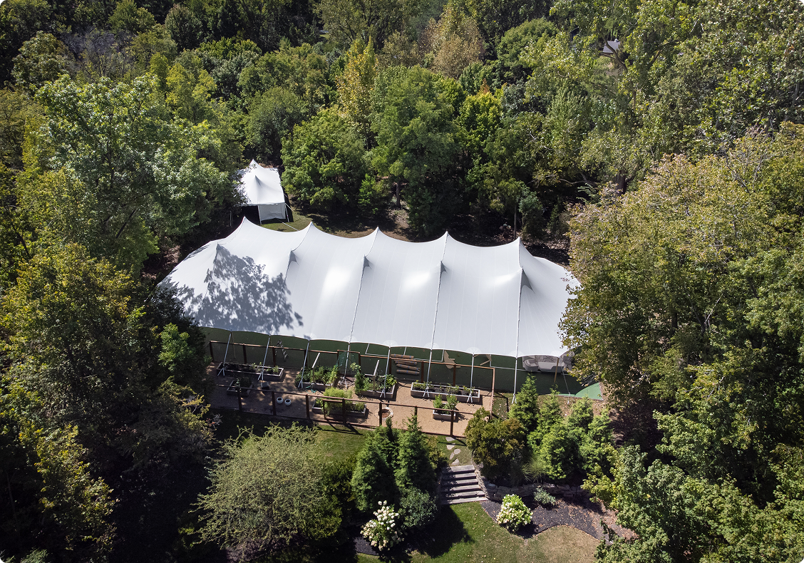 Large white event tent surrounded by trees in a forest clearing.