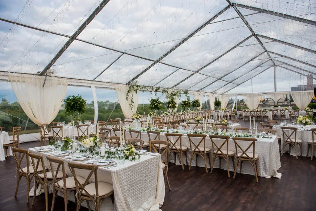 Clear wedding tent with white linens and scenic outdoor backdrop.