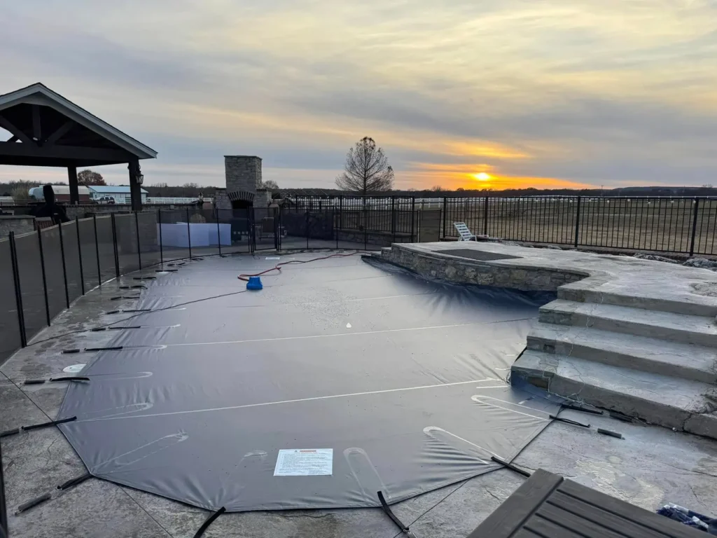 Dark blue safety pool cover near pavilion – Backyard pool with navy blue mesh cover, pavilion in background.