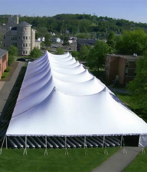 Long white multi-peak pole tent beside buildings.