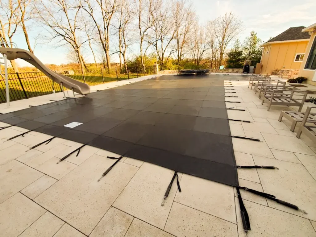 Black mesh safety pool cover – rectangular backyard pool with black safety cover secured by anchors.