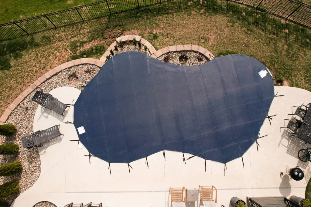 Dark gray mesh safety cover – irregular-shaped pool with fitted dark gray cover on stone deck.