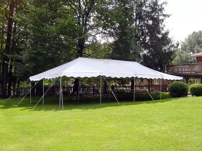 Classic white pole tent on a grassy lawn surrounded by trees.