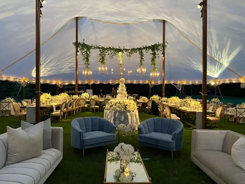 Luxurious event setup inside a clear tent with chandeliers and seating area.