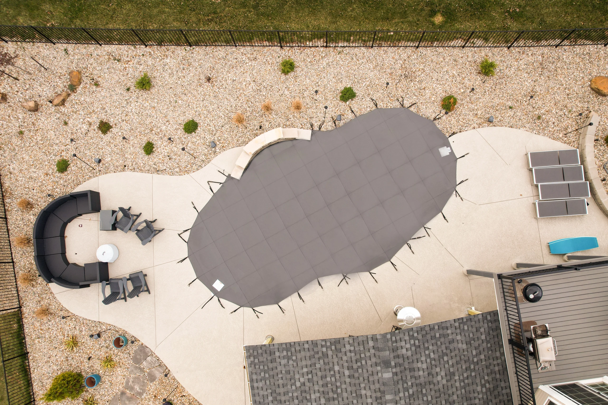 Overhead view of a custom-shaped gray safety pool cover on patio.