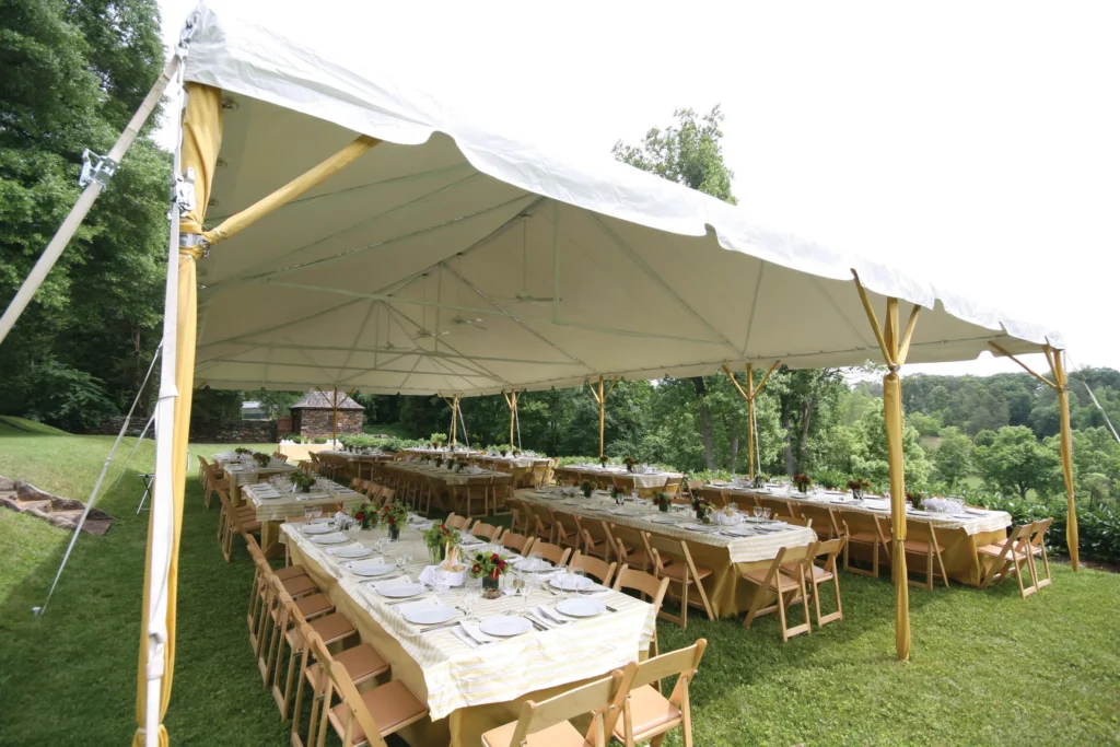 Open-sided tent with wooden tables arranged for an outdoor dinner.