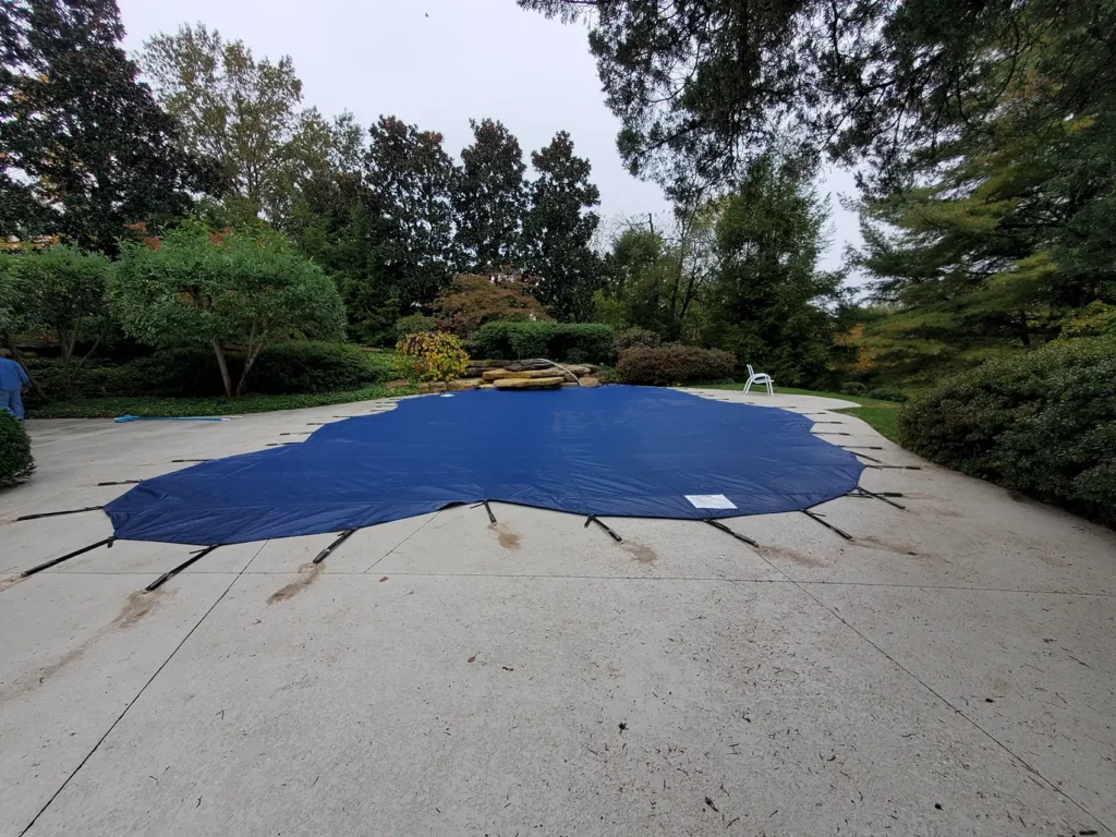Dark blue pool cover in wooded yard – pool surrounded by trees secured with dark blue safety mesh.