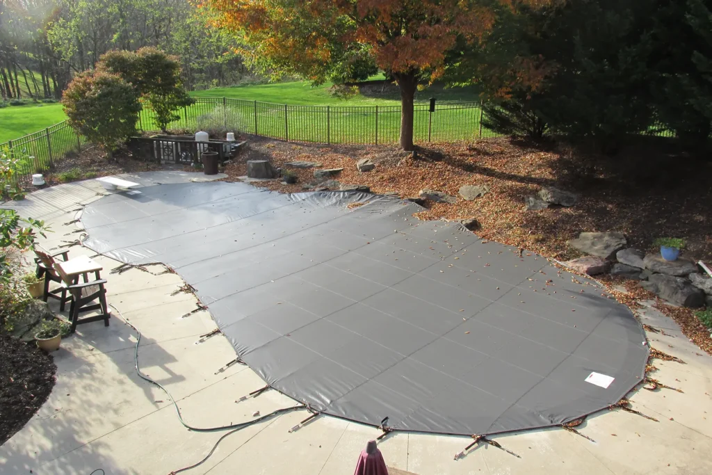 Backyard pool with a gray safety cover tightly fastened.