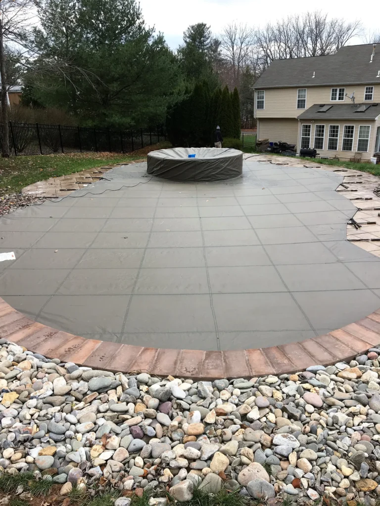Gray round pool safety cover bordered by stone landscaping.