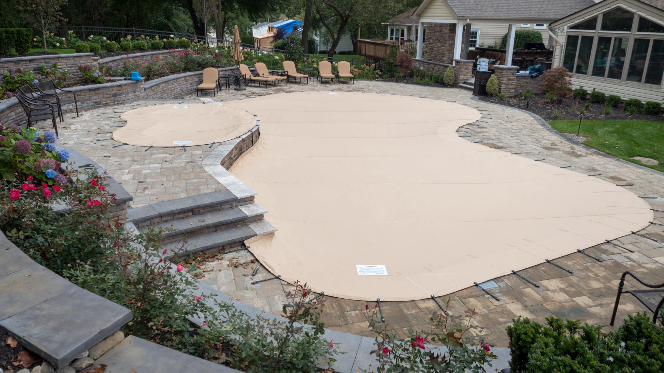 Tan safety pool cover installed over an inground backyard pool.
