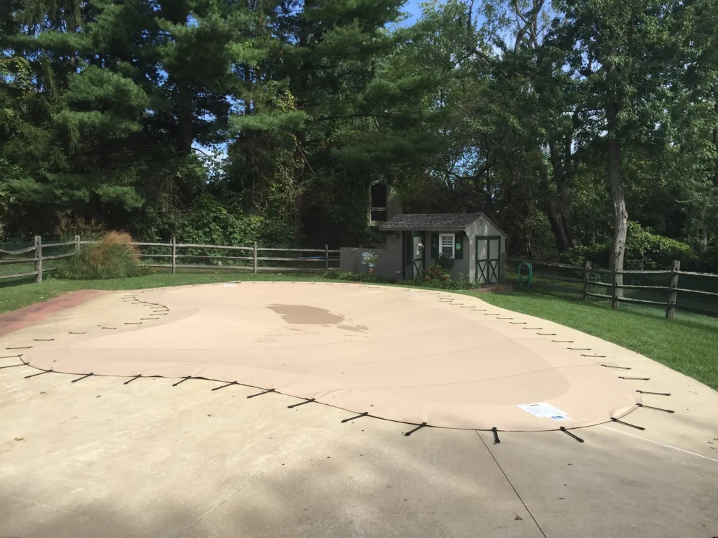 Beige pool safety cover stretched over an in-ground pool.