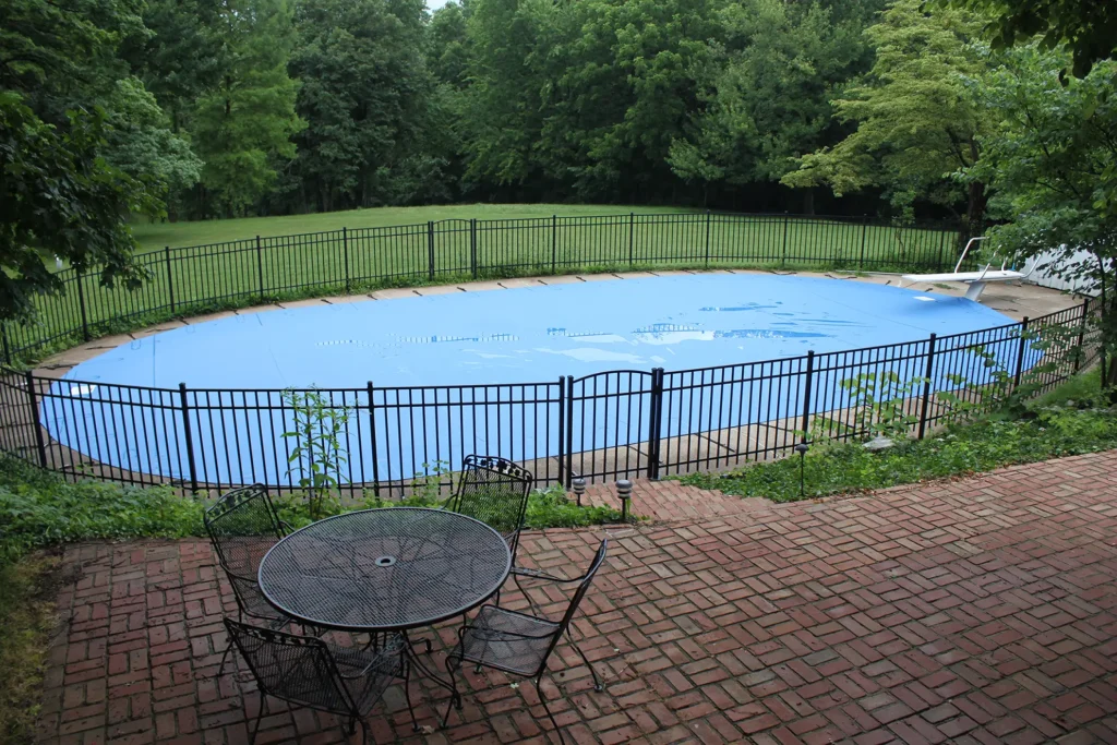Light blue pool cover secured on residential swimming pool with fence.