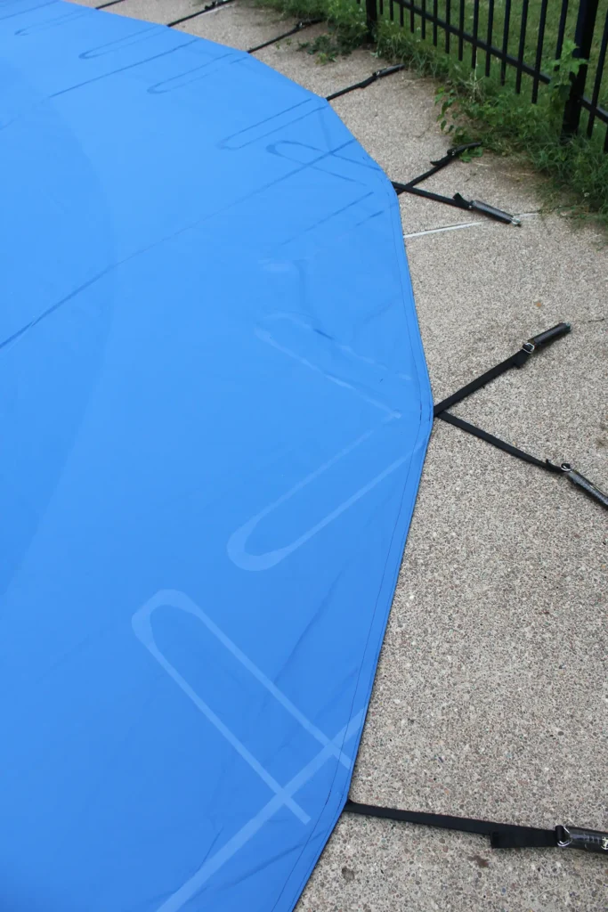 Blue safety pool cover stretched tightly across swimming pool deck.