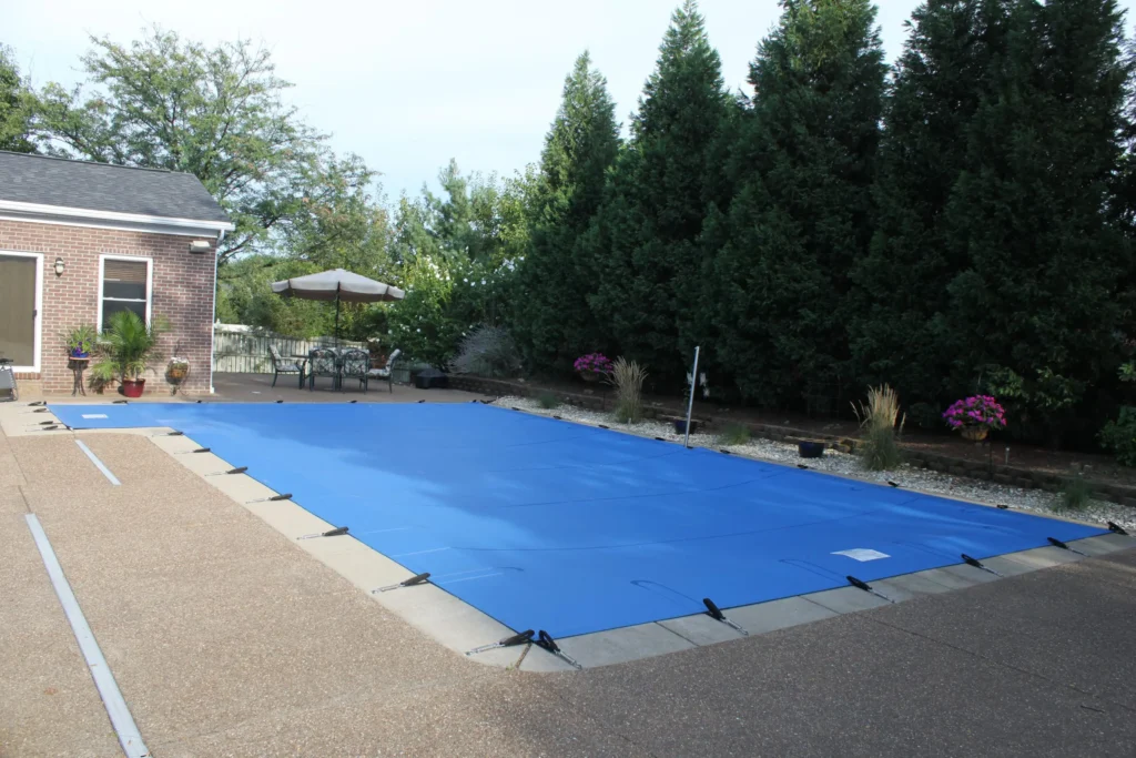Blue solid safety cover secured over rectangular pool in backyard