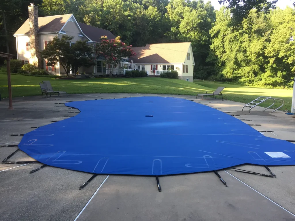 Blue safety cover secured over rectangular pool near house.