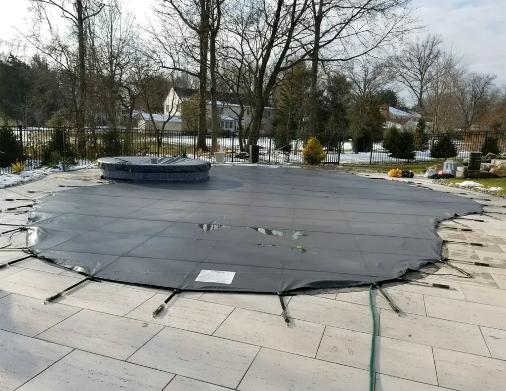 Black round pool safety cover installed on stone patio.