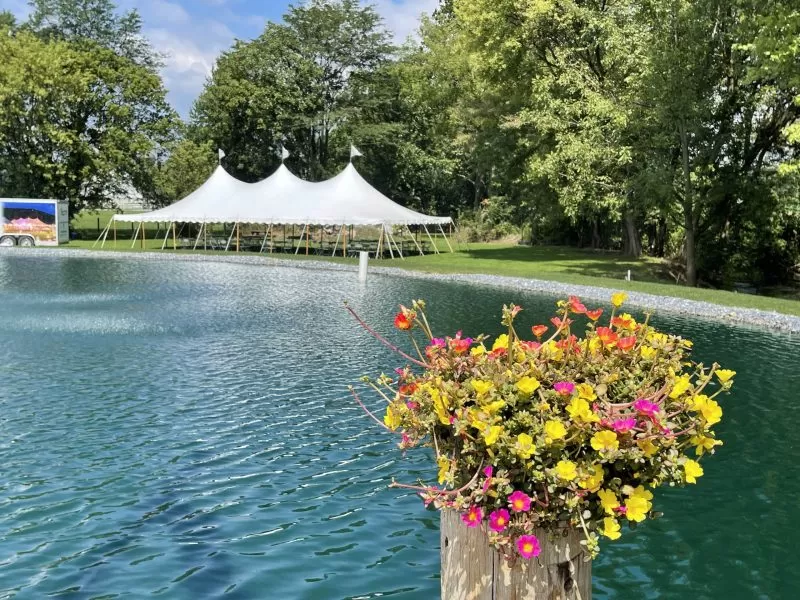 White event tent beside a pond with flower arrangement in foreground.