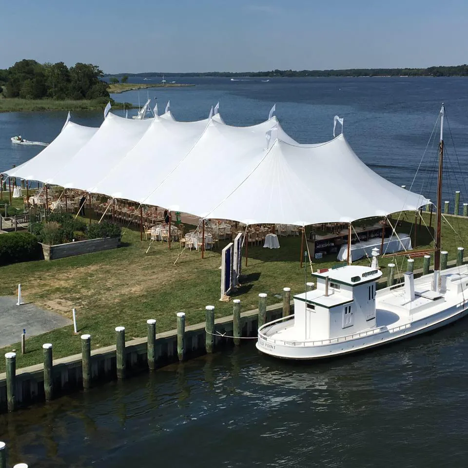 White event tent covering boats and guests along a lakeside dock.
