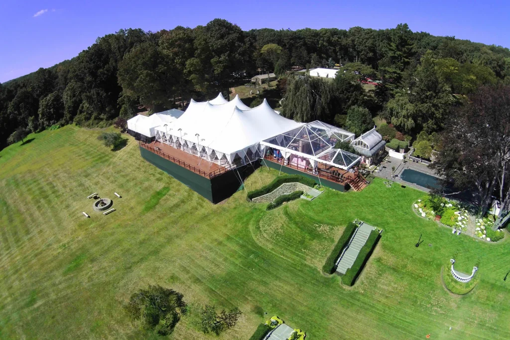 White event tent beside a building surrounded by trees and grass.