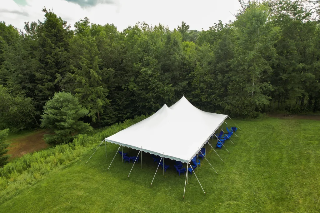Small white canopy tent surrounded by trees in a grassy field.