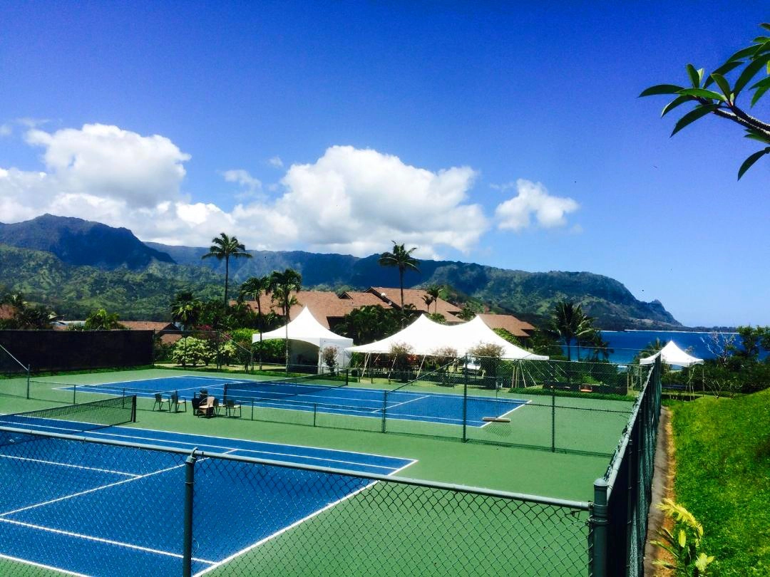 Outdoor event space with multiple Anchor Industries white tents near tennis courts