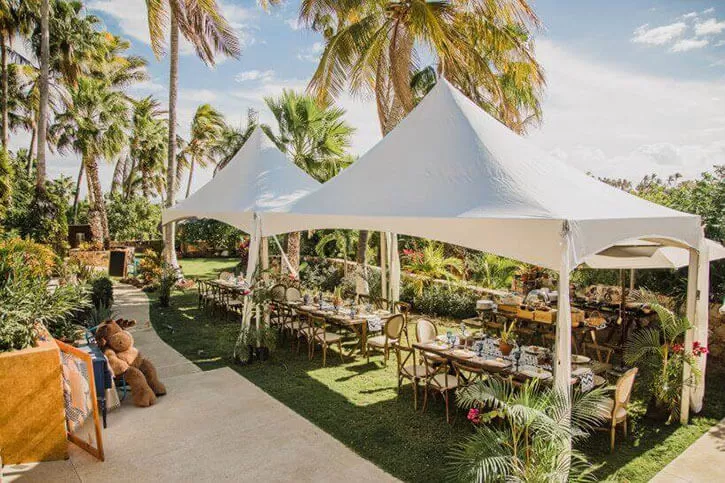 White high-peak tent shading rustic wooden tables for an outdoor celebration.